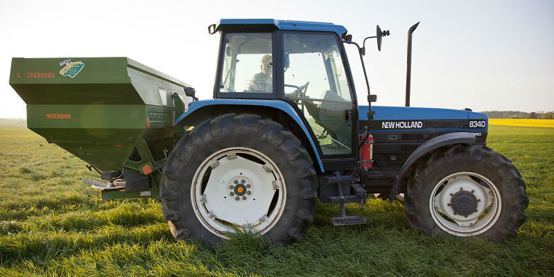 En blå traktor med mineralgödselspridare  i närbild på ett fält.